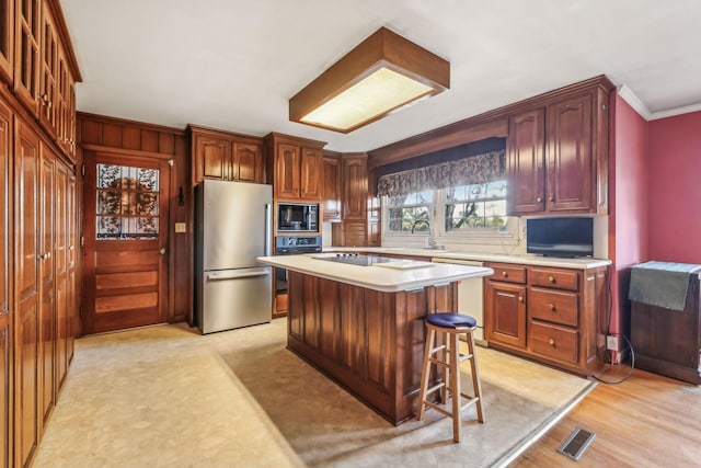 kitchen featuring light wood-type flooring, ornamental molding, black appliances, a center island, and a breakfast bar area