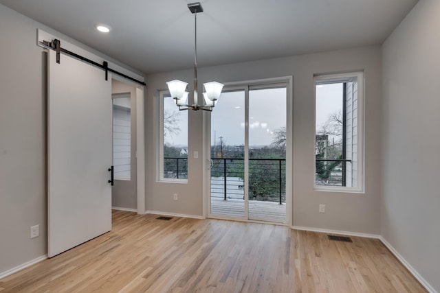 unfurnished dining area featuring a barn door, a chandelier, and light wood-type flooring