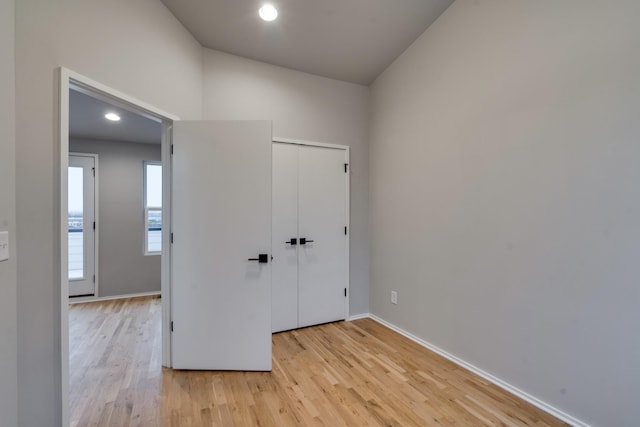 unfurnished bedroom with light hardwood / wood-style floors, lofted ceiling, and a closet