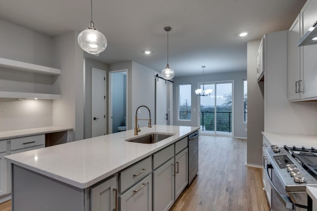 kitchen featuring sink, a barn door, light wood-type flooring, an island with sink, and stainless steel appliances