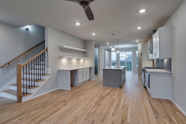 kitchen featuring decorative light fixtures, a center island with sink, light hardwood / wood-style floors, and stainless steel gas range