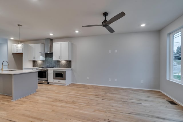 kitchen featuring white cabinetry, sink, wall chimney range hood, pendant lighting, and appliances with stainless steel finishes