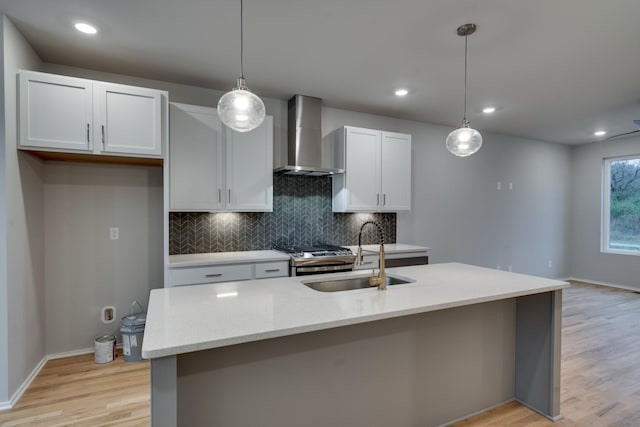 kitchen featuring sink, wall chimney exhaust hood, hanging light fixtures, and a center island with sink