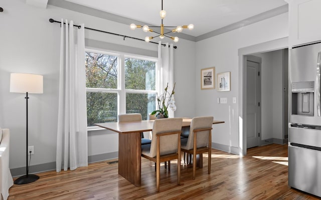 dining space with hardwood / wood-style floors, ornamental molding, and an inviting chandelier