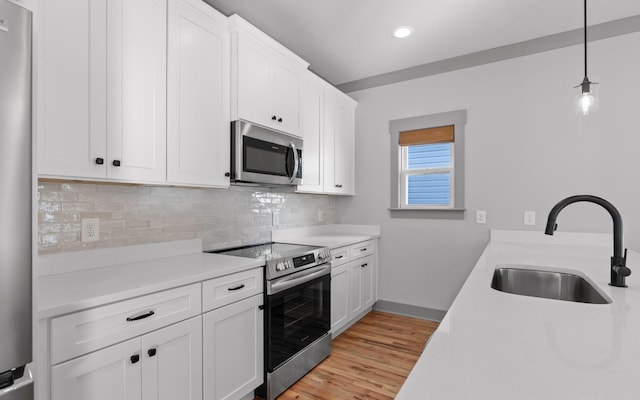 kitchen with white cabinetry, sink, hanging light fixtures, stainless steel appliances, and light wood-type flooring