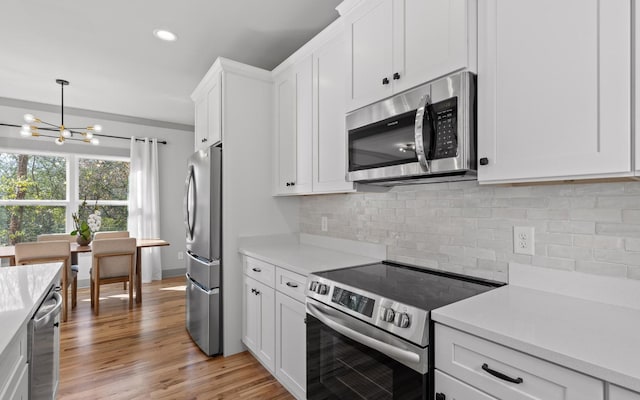 kitchen with light hardwood / wood-style flooring, decorative backsplash, appliances with stainless steel finishes, a notable chandelier, and white cabinetry