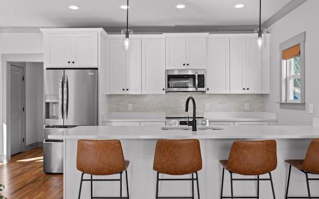 kitchen with appliances with stainless steel finishes, white cabinetry, pendant lighting, and an island with sink