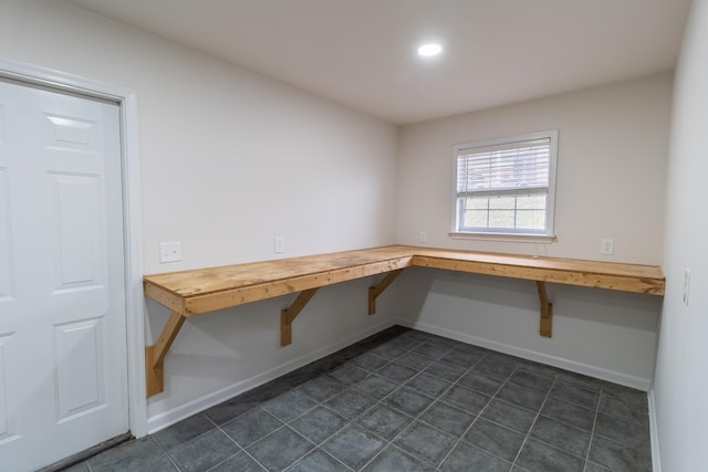 unfurnished office with dark tile patterned floors and built in desk