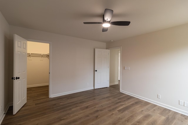 unfurnished bedroom with ceiling fan, a walk in closet, dark wood-type flooring, and a closet