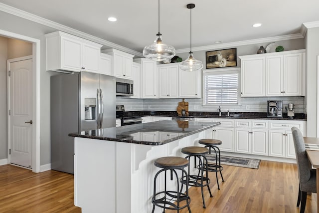 kitchen featuring appliances with stainless steel finishes, crown molding, white cabinets, light hardwood / wood-style floors, and a kitchen island