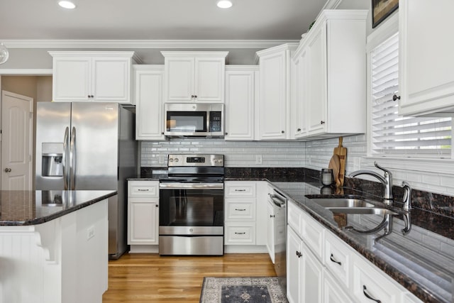 kitchen featuring white cabinets, appliances with stainless steel finishes, ornamental molding, and dark stone counters