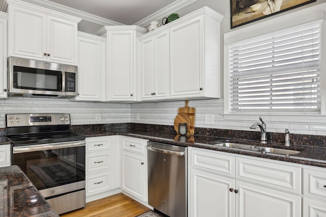 kitchen with sink, stainless steel appliances, crown molding, dark stone counters, and white cabinets