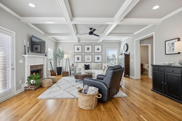 living room with ceiling fan, coffered ceiling, beamed ceiling, a fireplace, and light wood-type flooring