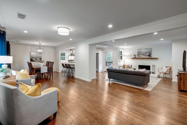 living room featuring hardwood / wood-style floors, ornamental molding, and a brick fireplace