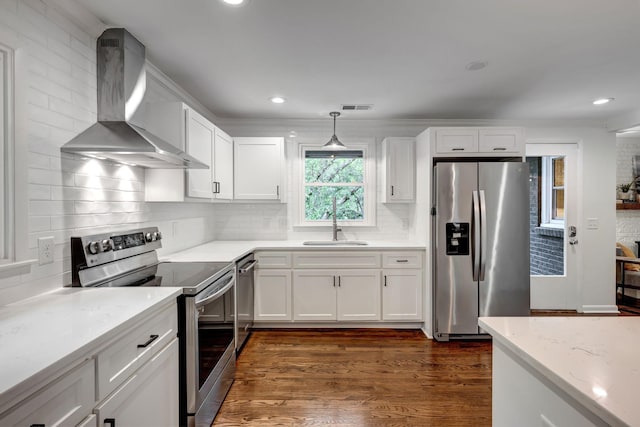 kitchen with wall chimney exhaust hood, stainless steel appliances, dark wood-type flooring, white cabinets, and hanging light fixtures