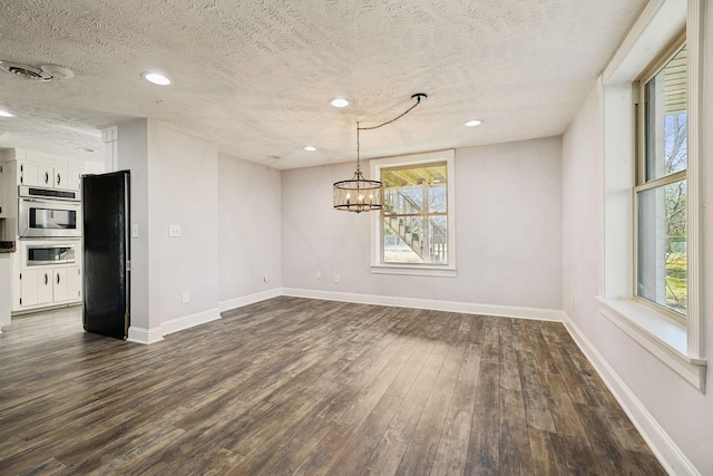 unfurnished dining area with dark hardwood / wood-style flooring, a textured ceiling, and an inviting chandelier