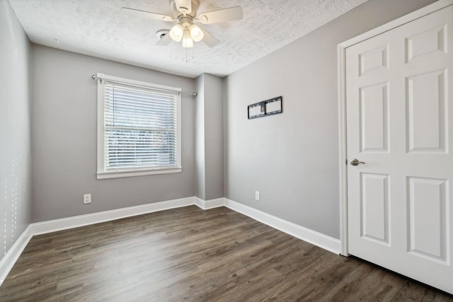 empty room with a textured ceiling, ceiling fan, and dark hardwood / wood-style floors