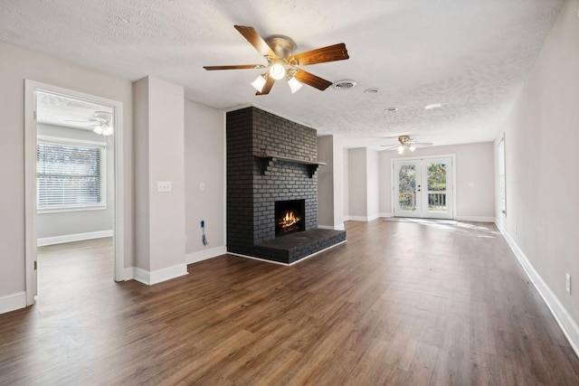 unfurnished living room with french doors, dark hardwood / wood-style flooring, a textured ceiling, and a brick fireplace