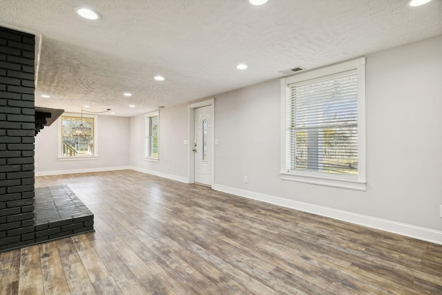 unfurnished living room with a chandelier, wood-type flooring, a textured ceiling, and a brick fireplace