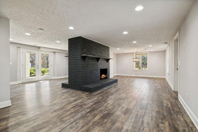 unfurnished living room with french doors, dark hardwood / wood-style flooring, a textured ceiling, and a brick fireplace