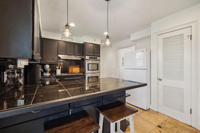 kitchen with a breakfast bar, light tile patterned floors, appliances with stainless steel finishes, decorative light fixtures, and dark brown cabinetry