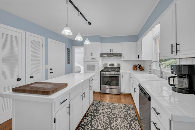 kitchen with appliances with stainless steel finishes, backsplash, a kitchen island, sink, and white cabinetry