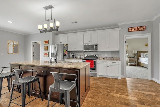 kitchen featuring white cabinets, a center island with sink, hardwood / wood-style flooring, light stone countertops, and stainless steel appliances