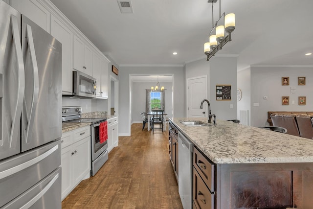 kitchen featuring hanging light fixtures, appliances with stainless steel finishes, an island with sink, white cabinets, and hardwood / wood-style flooring