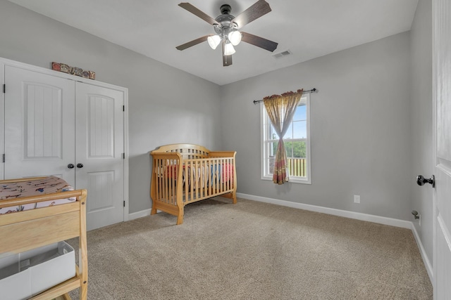 carpeted bedroom featuring a crib, a closet, and ceiling fan