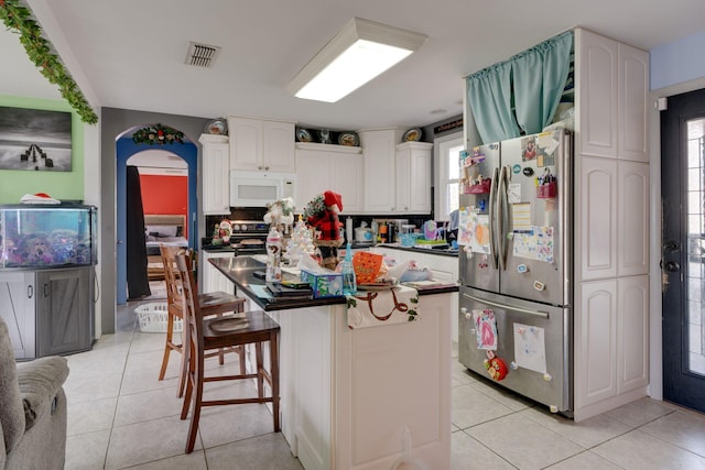 kitchen with white cabinetry, light tile patterned flooring, stainless steel fridge, a kitchen bar, and a kitchen island