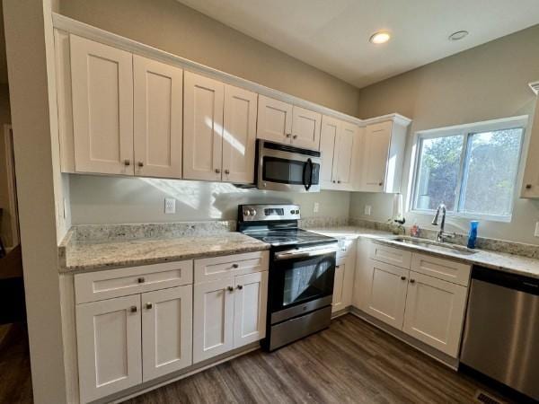 kitchen with appliances with stainless steel finishes, dark hardwood / wood-style flooring, light stone counters, sink, and white cabinets