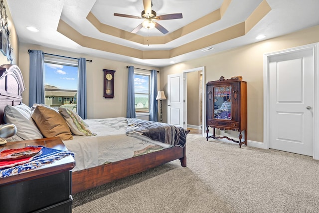 carpeted bedroom with ceiling fan and a tray ceiling