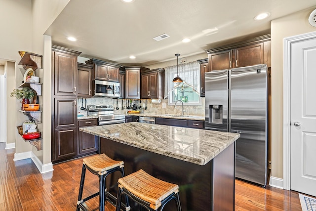 kitchen with dark hardwood / wood-style flooring, stainless steel appliances, sink, a center island, and hanging light fixtures