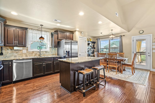 kitchen with appliances with stainless steel finishes, a center island, hanging light fixtures, and dark wood-type flooring