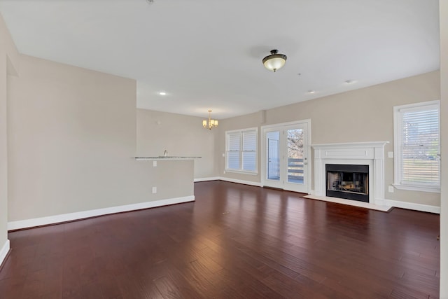 unfurnished living room with plenty of natural light, dark wood-type flooring, and a notable chandelier