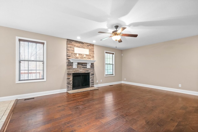 unfurnished living room featuring dark hardwood / wood-style floors, a stone fireplace, a wealth of natural light, and ceiling fan