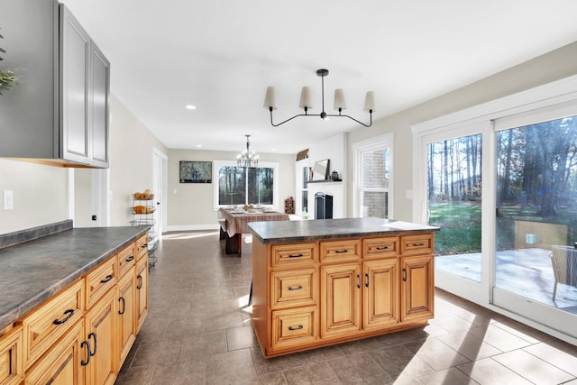 kitchen with pendant lighting, a center island, dark tile patterned flooring, a brick fireplace, and a notable chandelier