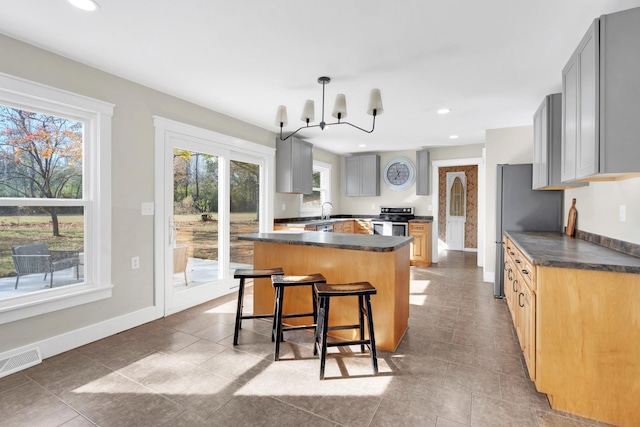 kitchen with an inviting chandelier, pendant lighting, gray cabinets, a kitchen island, and appliances with stainless steel finishes