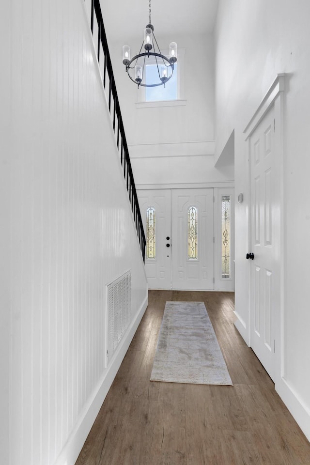 entryway featuring a towering ceiling, dark wood-type flooring, and a notable chandelier