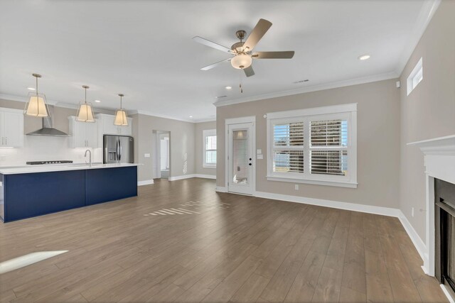 unfurnished living room featuring sink, wood-type flooring, and ornamental molding