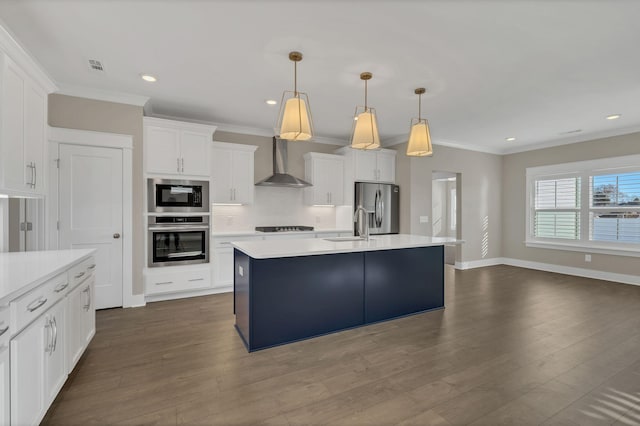 kitchen with white cabinets, decorative light fixtures, wall chimney range hood, and appliances with stainless steel finishes