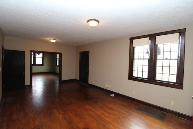 unfurnished room with a textured ceiling, a healthy amount of sunlight, and dark hardwood / wood-style floors