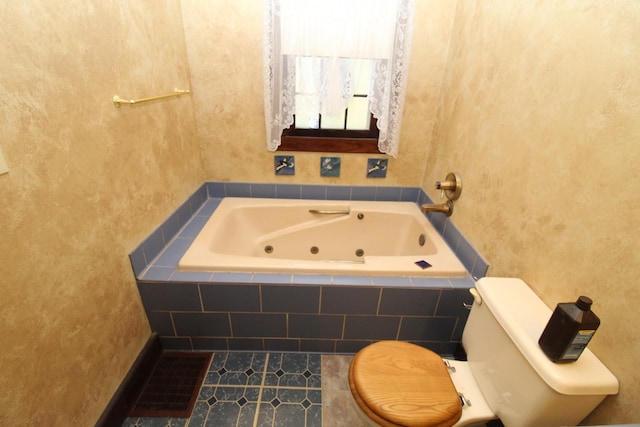 bathroom featuring tile patterned flooring, a relaxing tiled tub, and toilet