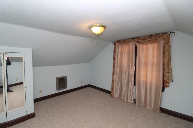 additional living space with a textured ceiling, heating unit, light colored carpet, and vaulted ceiling