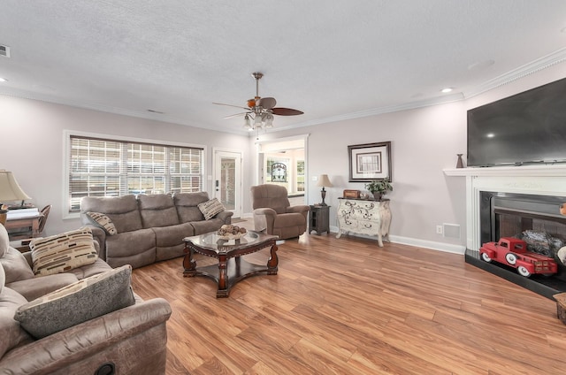 living room with a textured ceiling, light wood-type flooring, ceiling fan, and crown molding