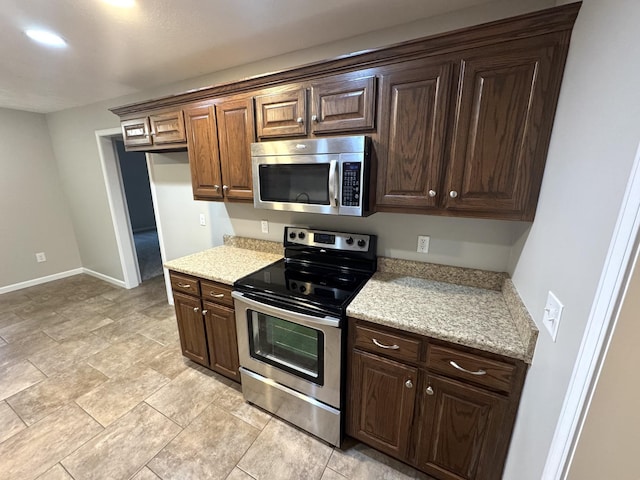 kitchen featuring dark brown cabinets, light stone countertops, and stainless steel appliances