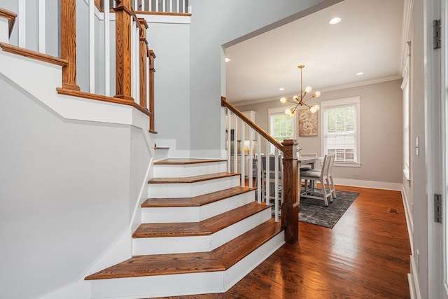 stairs with crown molding, wood-type flooring, and an inviting chandelier