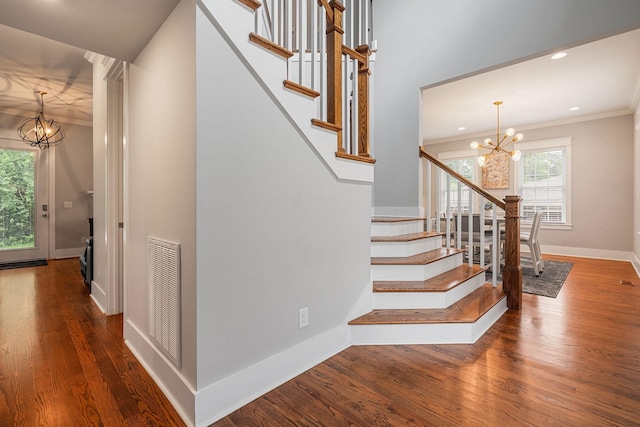 staircase featuring wood-type flooring, an inviting chandelier, and crown molding