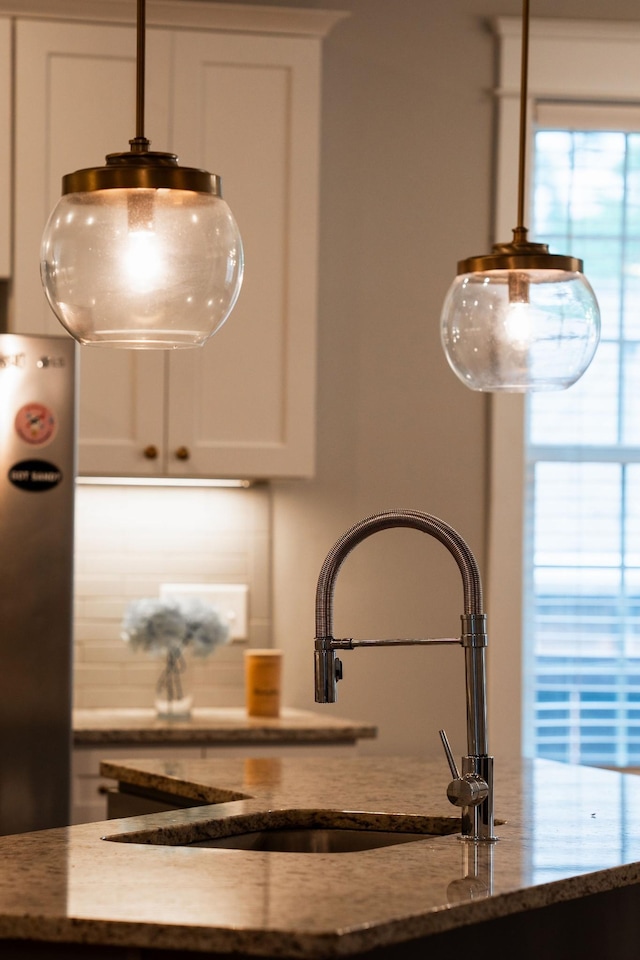 room details featuring sink, white cabinetry, stainless steel refrigerator, and dark stone countertops