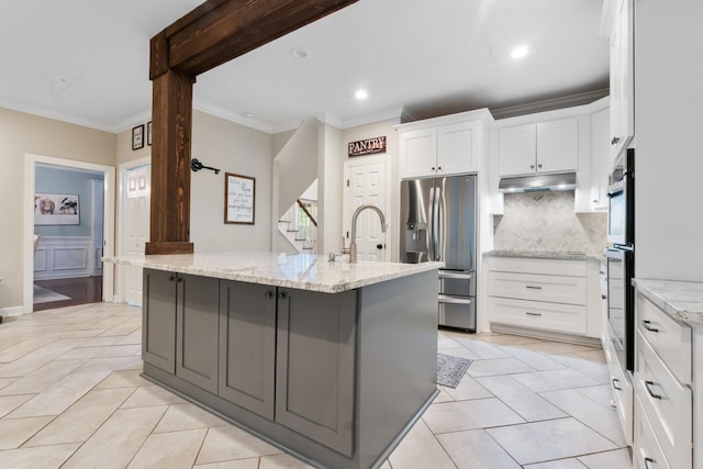 kitchen with white cabinetry, light stone countertops, stainless steel refrigerator with ice dispenser, a center island with sink, and ornamental molding